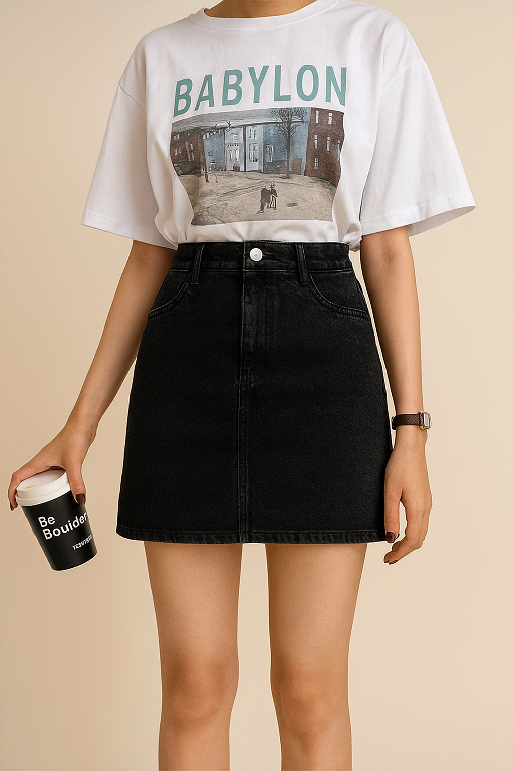 Person wearing a white t-shirt with 'BABYLON' print and a black skirt, holding a coffee cup.