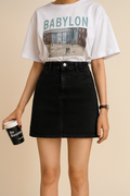 Person wearing a white t-shirt with 'BABYLON' print and a black skirt, holding a coffee cup.