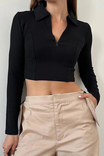 Person wearing a black long-sleeve crop top and beige pants against a plain background