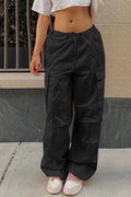 Person wearing black cargo pants and pink shoes standing on a sidewalk.